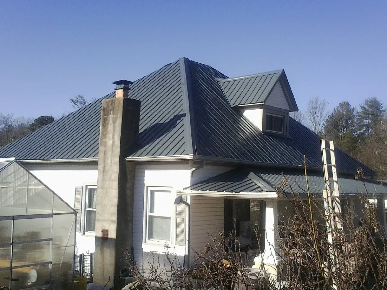Dark blue standing seam metal roof on a white farmhouse with dormer — Slate & Tile Roof Repair by Roofing Brothers in Longwood