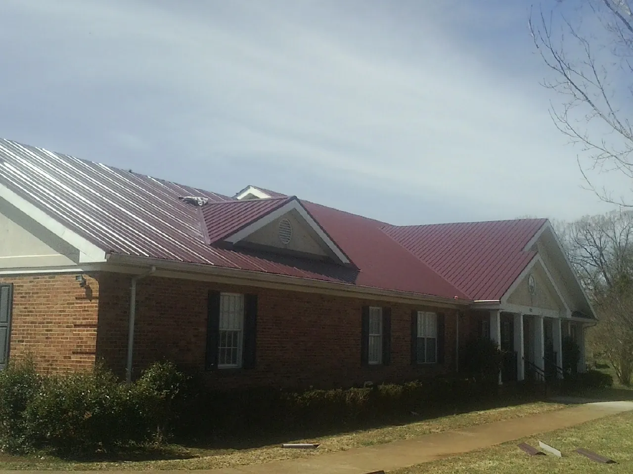Red metal roof with gabled entries on a long brick building, from a Hail Damage Roof Repair job in Longwood