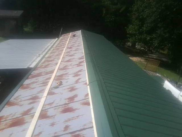 Old rusted panels beside newly installed green metal roofing — Wind Damage Roof Repair by Roofing Brothers in Longwood