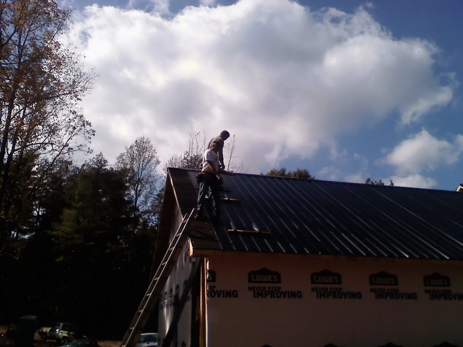 Roofer fastening dark metal panels high against a cloudy sky, from a Roof Inspection job in Longwood